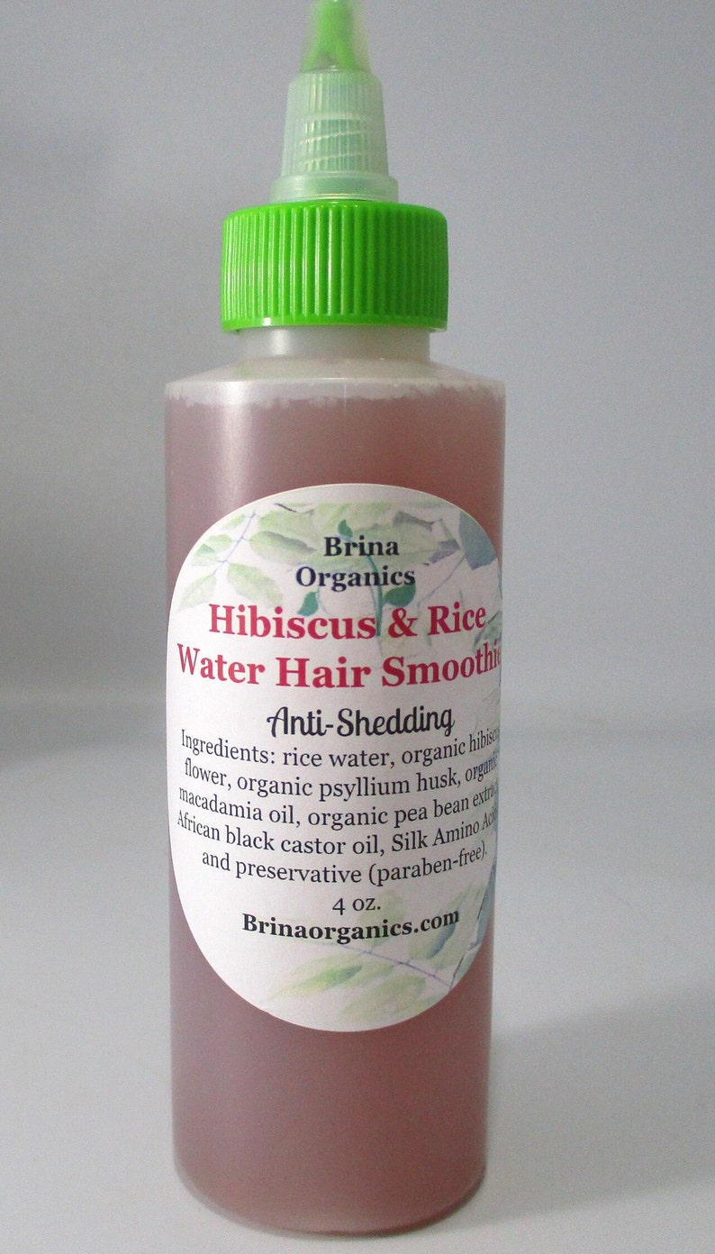 May include: A clear plastic squeeze bottle with a bright green cap containing a pink liquid. The label reads Brina Organics Hibiscus & Rice Water Hair Smoothie, Anti-Shedding, listing ingredients and 4 oz. volume, with a botanical leaf design.
