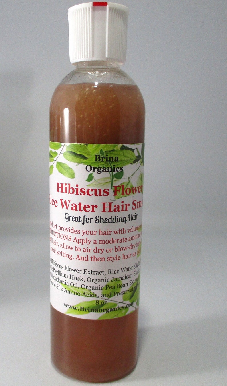 May include: A clear plastic bottle filled with a brownish liquid, topped with a white cap. The label reads Brina Organics Hibiscus Flower Rice Water Hair Smoothie, Great for Shedding Hair, and lists ingredients including 8 oz. net weight.