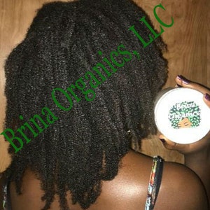 May include: A round white container with a label featuring a green graphic of a person with curly hair and the text Brina Organics. The container is held near dark, textured, curly hair that falls to the shoulders, with the text Brina Organics, LLC.