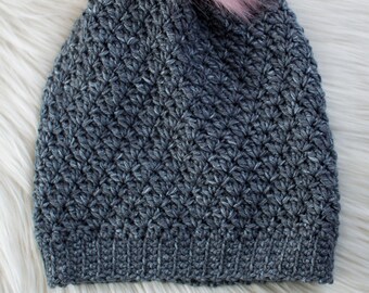 May include: A gray crocheted beanie with a pink faux fur pom pom.