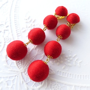 Peut inclure: Une paire de boucles d'oreilles en forme de boule de tissu rouge avec des maillons de chaîne dorés et des fermoirs à clip.