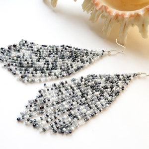 May include: A pair of long, silver dangle earrings with black and white beads. The earrings are made of small, round beads that are strung together in a cascading pattern.