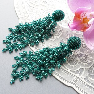 May include: A pair of teal blue beaded tassel earrings. The earrings are long and dangle, with a cluster of beads at the top and a fringe of beads hanging down.