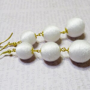 Op de afbeelding: Witte stoffen bal oorbellen met gouden haken en verbindingsringen. De oorbellen zijn gemaakt van meerdere stoffen ballen.