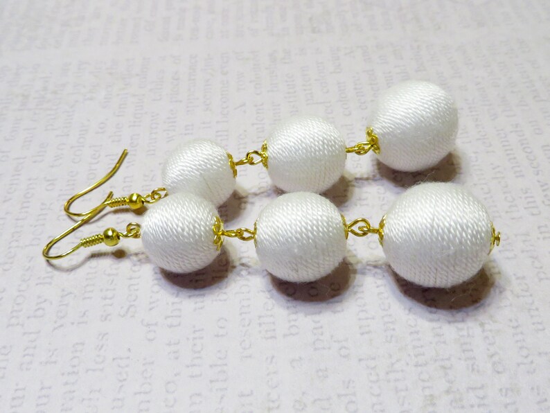 Op de afbeelding: Witte stoffen bal oorbellen met gouden haken en verbindingsringen. De oorbellen zijn gemaakt van meerdere stoffen ballen.