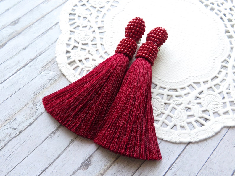 May include: A pair of long, red tassel earrings with beaded tops. The tassels are made of a soft, silky material and hang down to about 3 inches in length.