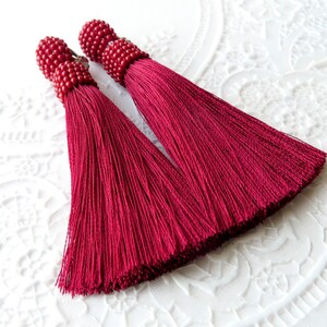 May include: A pair of long, burgundy tassel earrings with red bead accents.