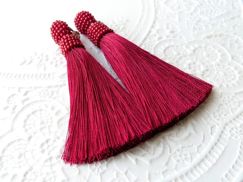 May include: A pair of long, burgundy tassel earrings with red bead accents.