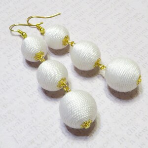 Op de afbeelding: Witte zijden kwast oorbellen met gouden accenten. De oorbellen hebben aan elke kant drie ronde zijden ballen.