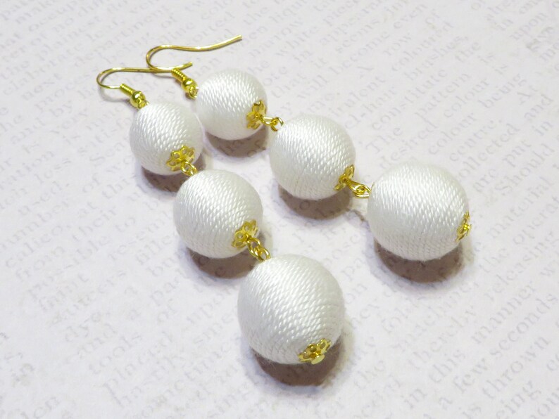 Op de afbeelding: Witte zijden kwast oorbellen met gouden accenten. De oorbellen hebben aan elke kant drie ronde zijden ballen.