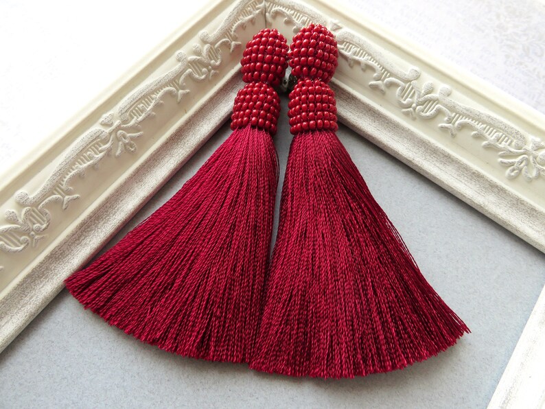 May include: A pair of long, red tassel earrings with beaded tops. The tassels are made of a soft, silky material and hang down to about 3 inches in length.