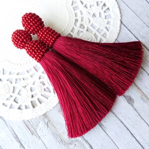 May include: A pair of red tassel earrings with beaded tops. The tassels are made of a soft, silky fabric and are about 3 inches long.