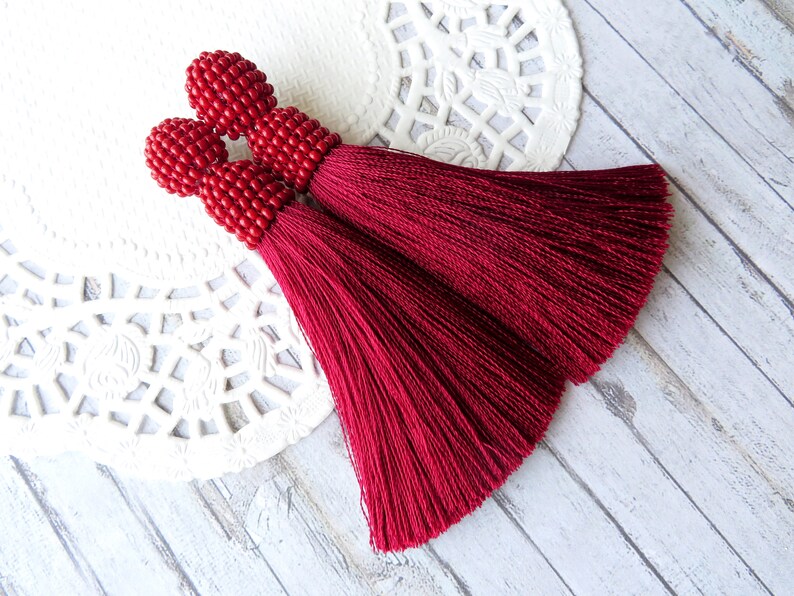 May include: A pair of red tassel earrings with beaded tops. The tassels are made of a soft, silky fabric and are about 3 inches long.