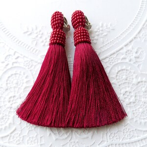 May include: A pair of red tassel earrings with a clip-on closure. The tassels are made of a soft, silky material and are about 2 inches long.
