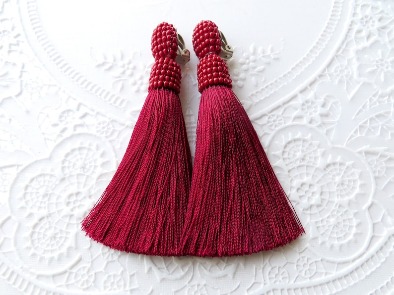 May include: A pair of red tassel earrings with a clip-on closure. The tassels are made of a soft, silky material and are about 2 inches long.