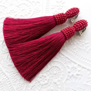 May include: A pair of crimson red tassel earrings with beaded tops and silver clip-on closures.