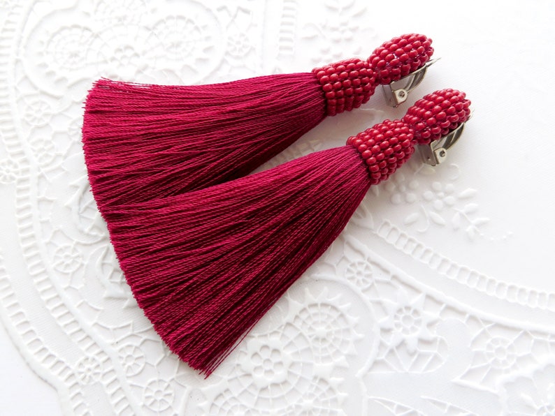 May include: A pair of crimson red tassel earrings with beaded tops and silver clip-on closures.