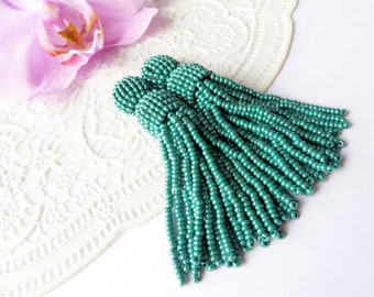 May include: A pair of teal blue beaded tassel earrings. The earrings are made of small, round beads that are strung together to create a long, flowing tassel.