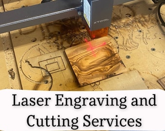 May include: A laser engraving and cutting machine with a red laser beam focused on a piece of wood. The machine is on a wooden table with the text "Laser Engraving and Cutting Services" on the table.