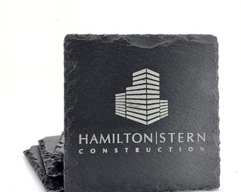 以下が含まれることがあります： 建物と「HAMILTON STERN CONSTRUCTION」のテキストが白で刻印された、黒いスレート製のコースター4枚セットです。