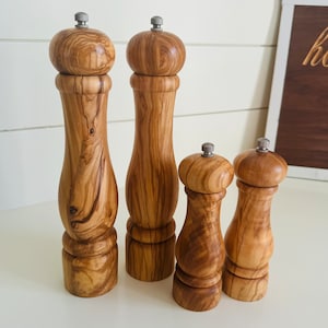 May include: Set of four wooden salt and pepper shakers with a natural wood grain finish. The shakers are different sizes and have a classic design.