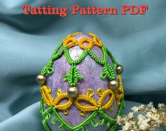 May include: A purple egg decorated with green and yellow shuttle tatting. The egg is surrounded by a light blue background and a small bouquet of white flowers.