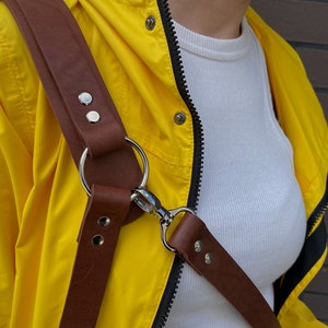 May include: A brown leather camera strap with silver hardware and two adjustable rings. The strap is worn over a yellow jacket.