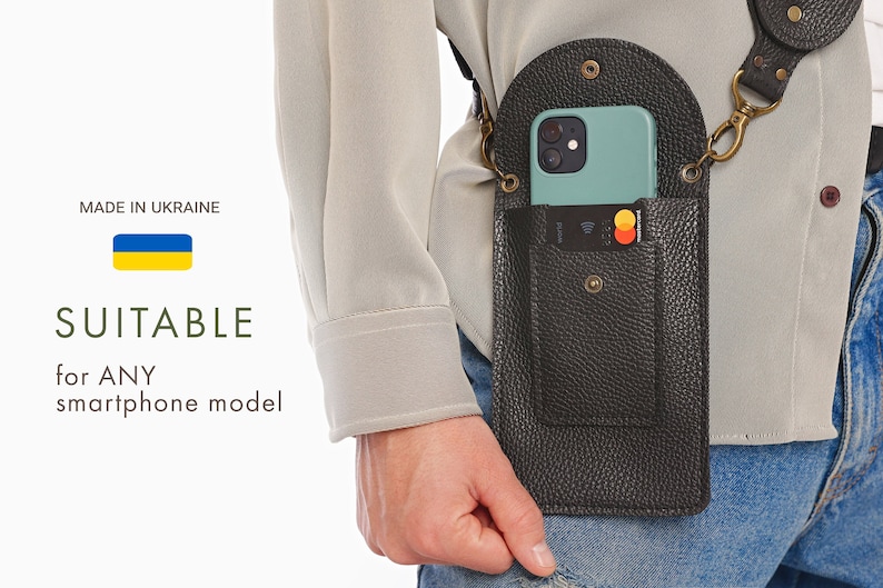 May include: A black leather phone holster with a strap and a pocket for cards. The phone holster is worn on a person's hip. The phone is light blue and has a black case. The phone holster is made in Ukraine.