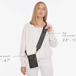 May include: A black crossbody bag with a phone pouch measuring 6.6 inches by 4.7 inches and a wide shoulder strap featuring a flat zip pocket measuring 2.5 inches by 11 inches. The bag has a snap button closure and brass-toned hardware.