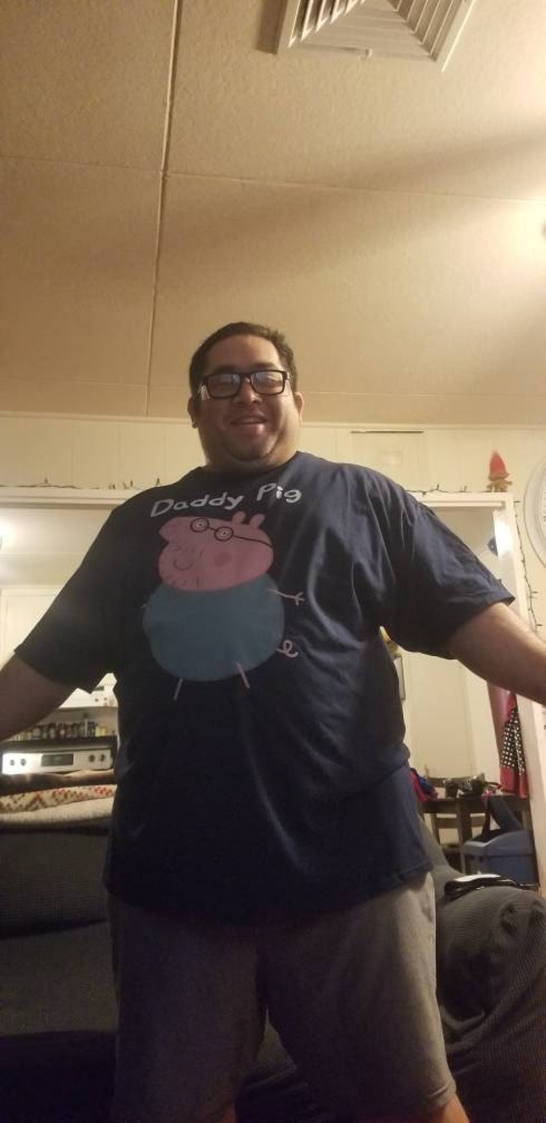 May include: A man wearing a navy blue t-shirt with a pink cartoon pig wearing glasses and the text "Daddy Pig".