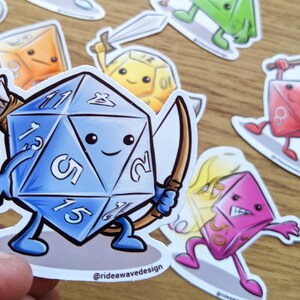 May include: A collection of colorful, cartoon-style stickers featuring various dice with faces and limbs, each holding a weapon or in action. The central sticker is a blue d20 die with a bow and arrow. The stickers are designed with a white border.