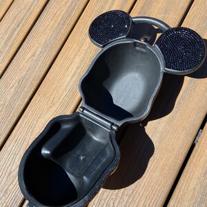 May include: A black purse shaped like Mickey Mouse's head, covered in rhinestones. The purse is open, showing a black interior.