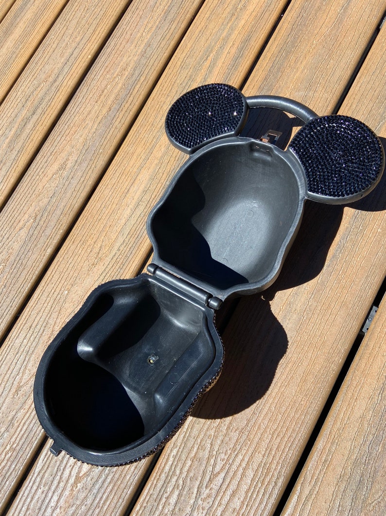 May include: A black purse shaped like Mickey Mouse's head, covered in rhinestones. The purse is open, showing a black interior.