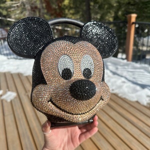 May include: A black and gold rhinestone-covered Mickey Mouse handbag with a black handle.