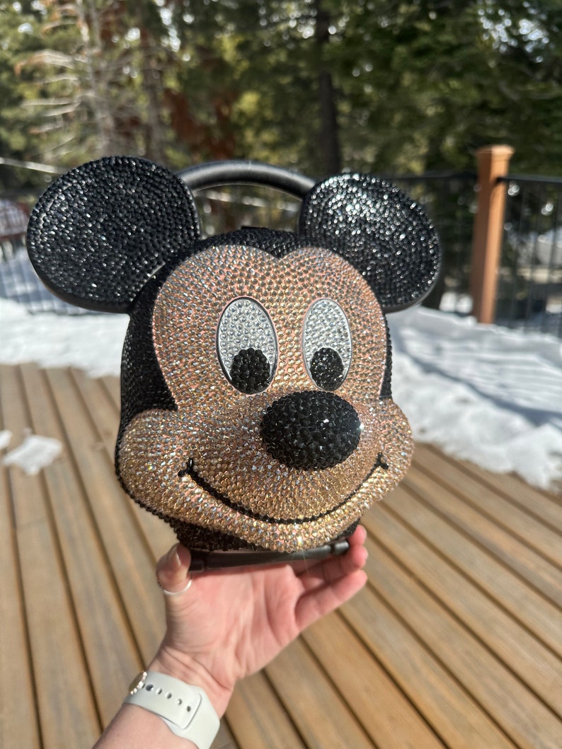 May include: A black and gold rhinestone-covered Mickey Mouse handbag with a black handle.