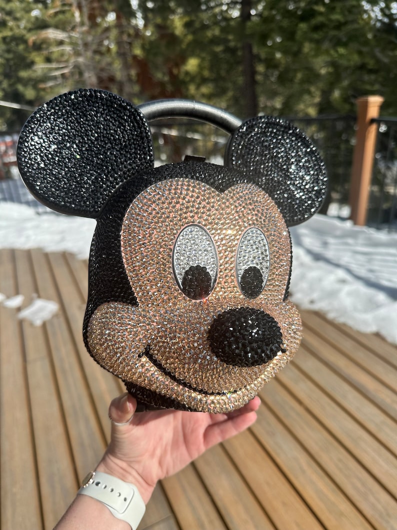 May include: A black and gold rhinestone-covered Mickey Mouse head handbag with a black handle.