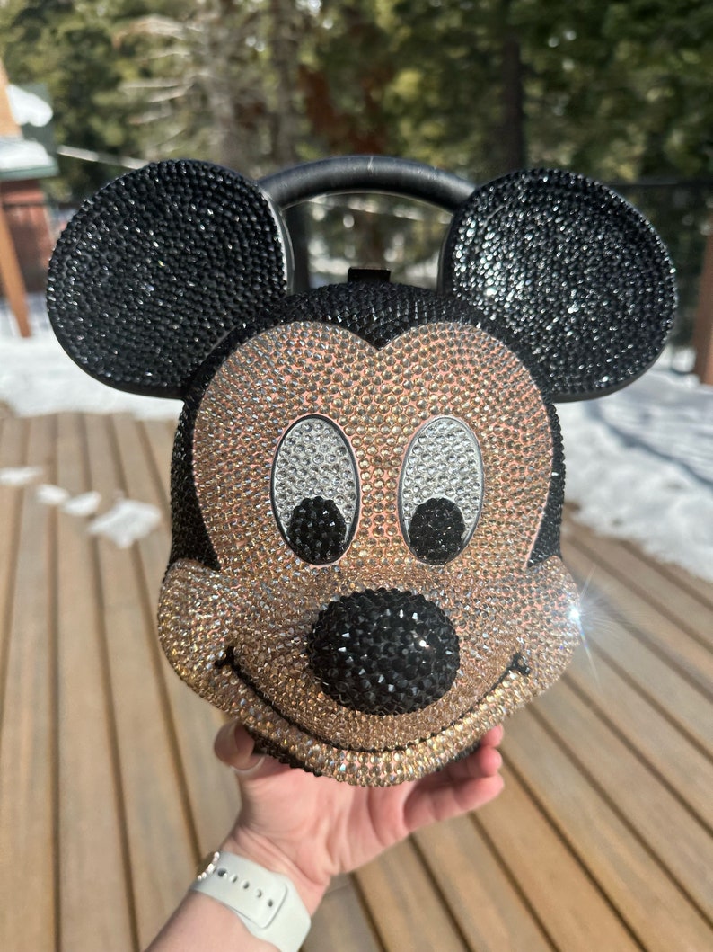 May include: A black and gold rhinestone-covered Mickey Mouse purse with a black handle.