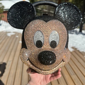 May include: A gold and black rhinestone-covered Mickey Mouse handbag with a black handle.
