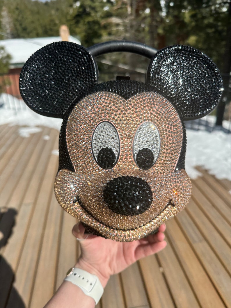 May include: A gold and black rhinestone-covered Mickey Mouse handbag with a black handle.
