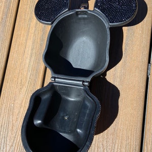 May include: Black purse shaped like Mickey Mouse's head with rhinestone ears. The purse is open and the inside is visible.