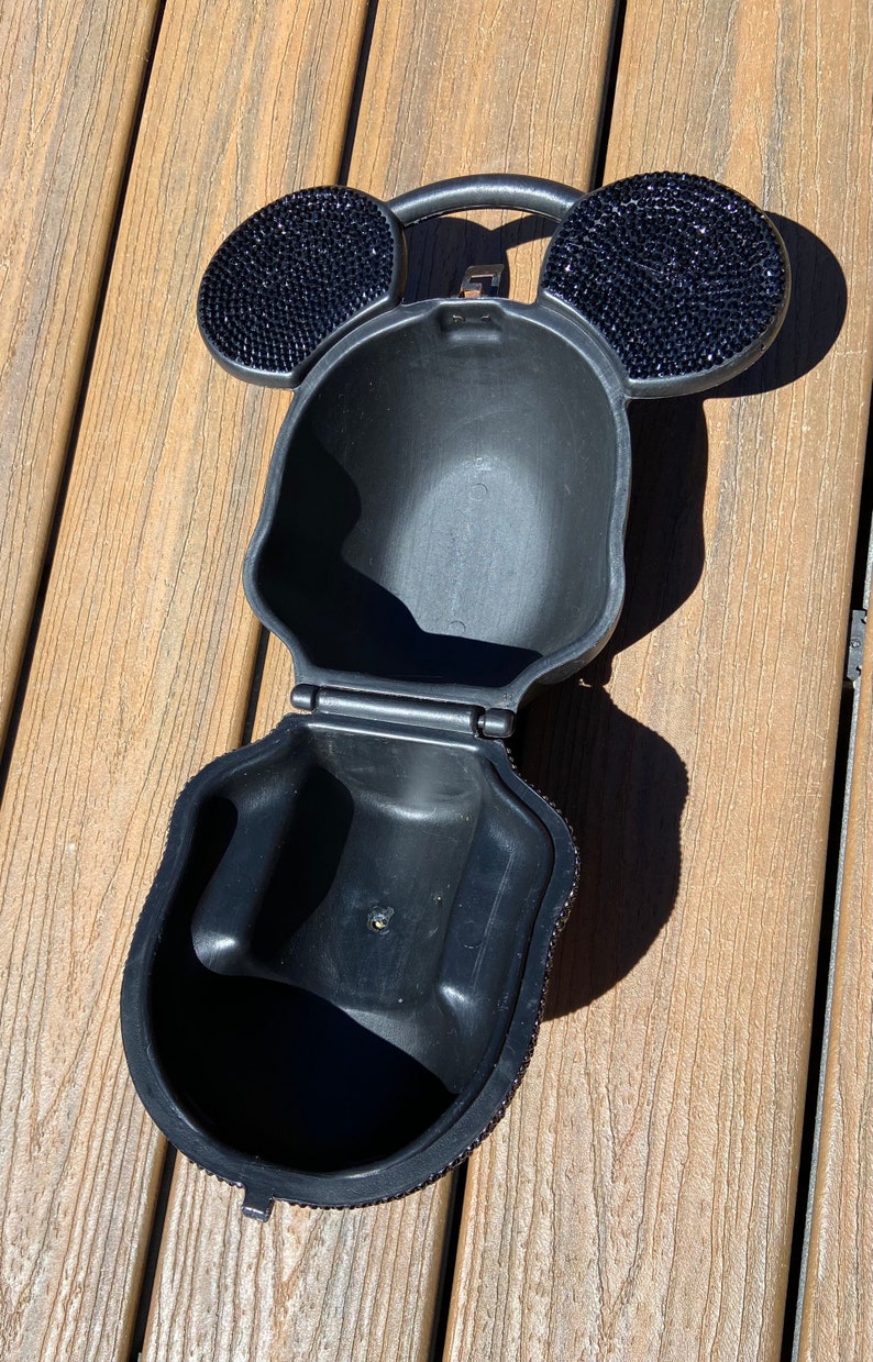 May include: Black purse shaped like Mickey Mouse's head with rhinestone ears. The purse is open and the inside is visible.