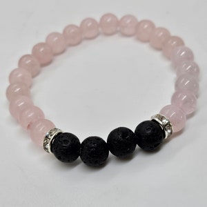 May include: A pink and black beaded bracelet with a silver spacer bead. The bracelet is made with rose quartz and lava rock beads.