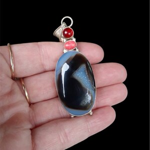 May include: A silver pendant with a large oval blue agate stone, accented with three smaller red and pink stones.