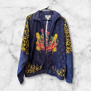 May include: A blue and gold patterned jacket with a zipper closure. The jacket features a large crest with lions and a crown. The text "Angel" is printed on the tag.