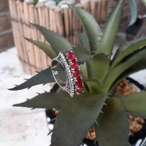 May include: A silver ring with a delicate filigree design and a row of red gemstones.