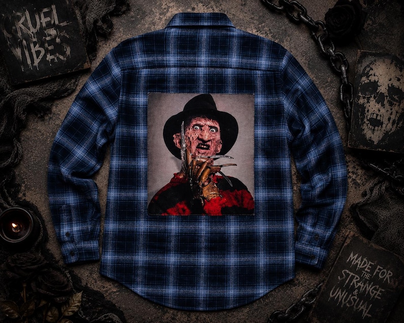 May include: A blue and black plaid long-sleeve button-down shirt featuring a large square graphic on the back. The graphic depicts a character wearing a dark fedora hat and a red and black striped sweater, with a metal clawed glove held near the face.