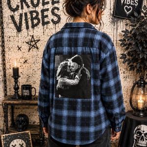 Puede incluir: Una camisa de manga larga con botones en un patr&oacute;n de cuadros azul y negro. La parte posterior de la camisa presenta un gran estampado gr&aacute;fico cuadrado en blanco y negro que representa a una pareja abraz&aacute;ndose. Tiene cuello y pu&ntilde;os abotonados.