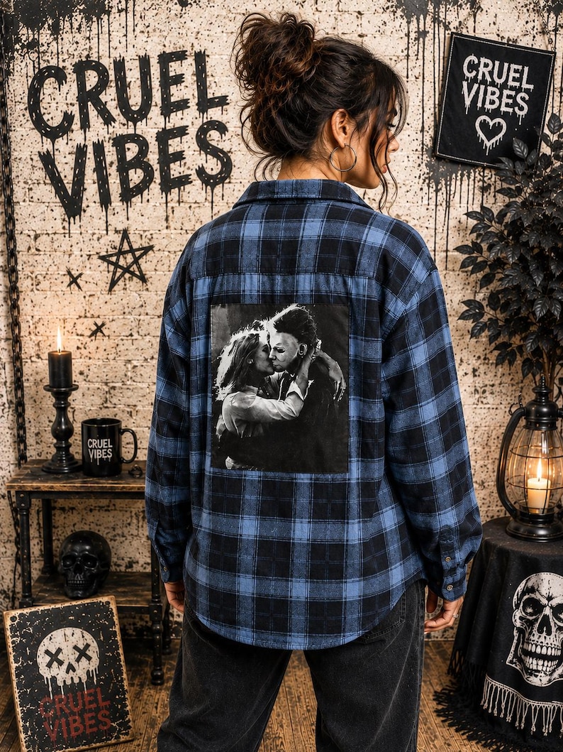 Puede incluir: Una camisa de manga larga con botones en un patr&oacute;n de cuadros azul y negro. La parte posterior de la camisa presenta un gran estampado gr&aacute;fico cuadrado en blanco y negro que representa a una pareja abraz&aacute;ndose. Tiene cuello y pu&ntilde;os abotonados.
