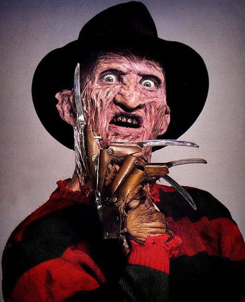 May include: A character with a scarred, textured face wearing a black fedora and a red and black horizontally striped sweater. The character has a metallic glove with long, sharp, curved blades attached to the fingers, positioned near the face.