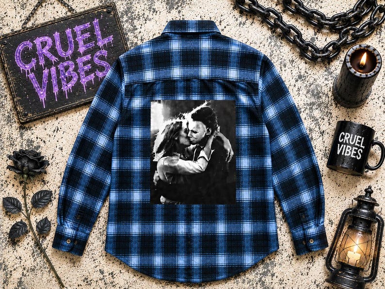 Puede incluir: Una camisa de manga larga con botones y un patr&oacute;n de cuadros en azul y negro. La parte posterior de la camisa muestra un estampado gr&aacute;fico en blanco y negro de una pareja abraz&aacute;ndose. La camisa tiene un cuello est&aacute;ndar y pu&ntilde;os abotonados.